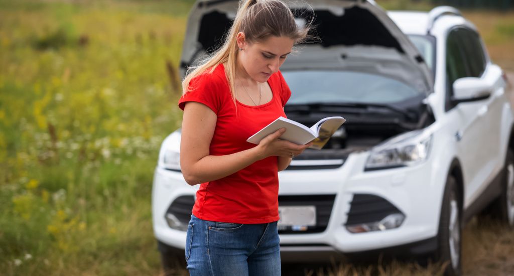 Woman reading her owners manual in front of her broken down car