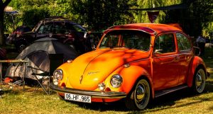Old orange Volkswagen beetle parked up next to tent