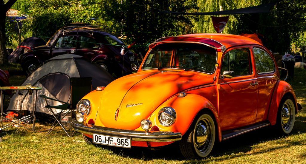 Old orange Volkswagen beetle parked up next to tent